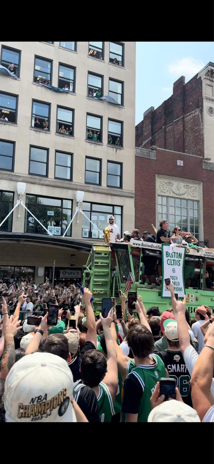 A group of people on a green truck with a crowd of people in the background

Description automatically generated