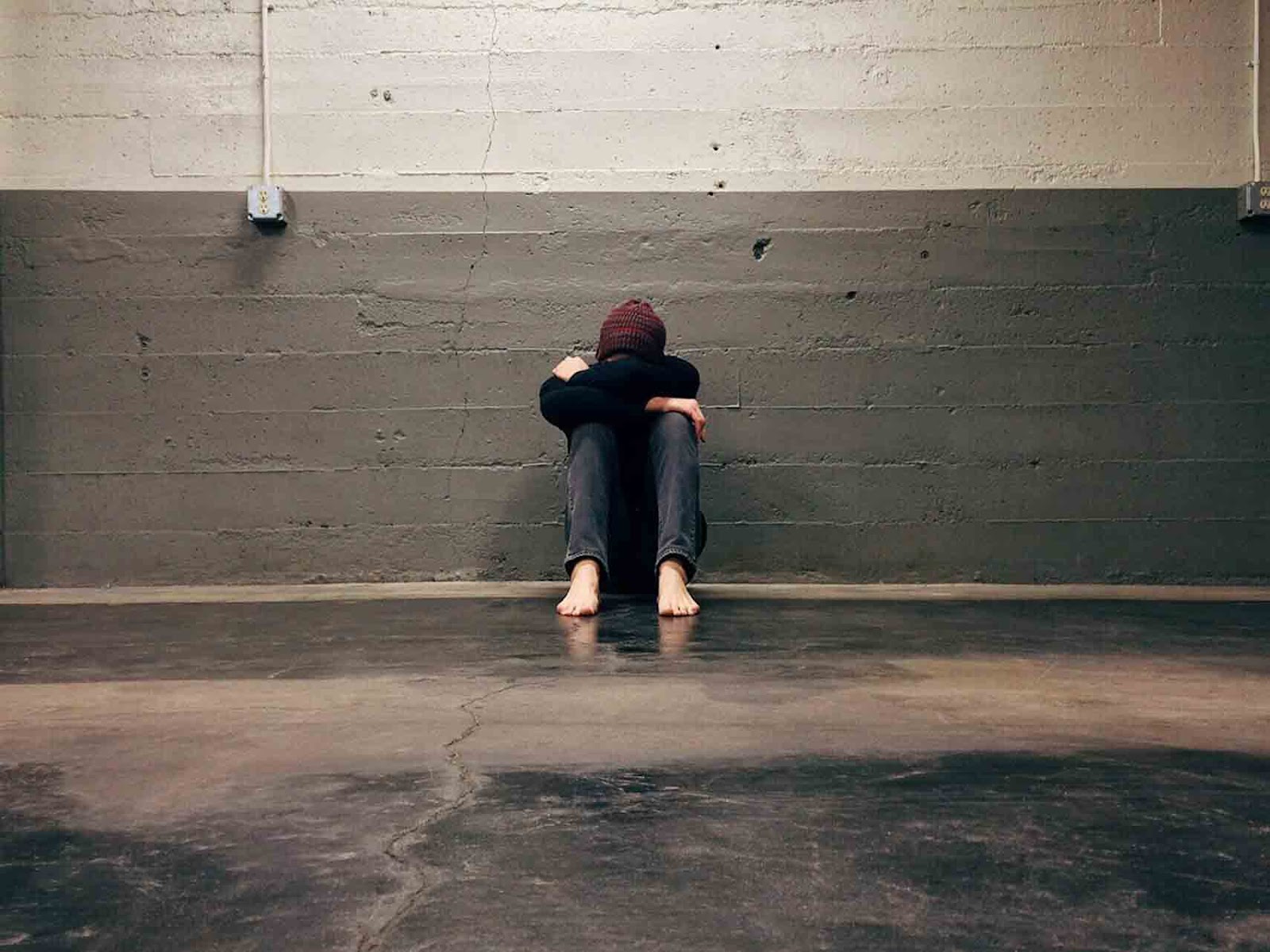 A person sitting on the floor against a concrete wall with their head buried in their arms, symbolizing emotional struggles and the challenges of obtaining short-term disability approval for anxiety and depression.
