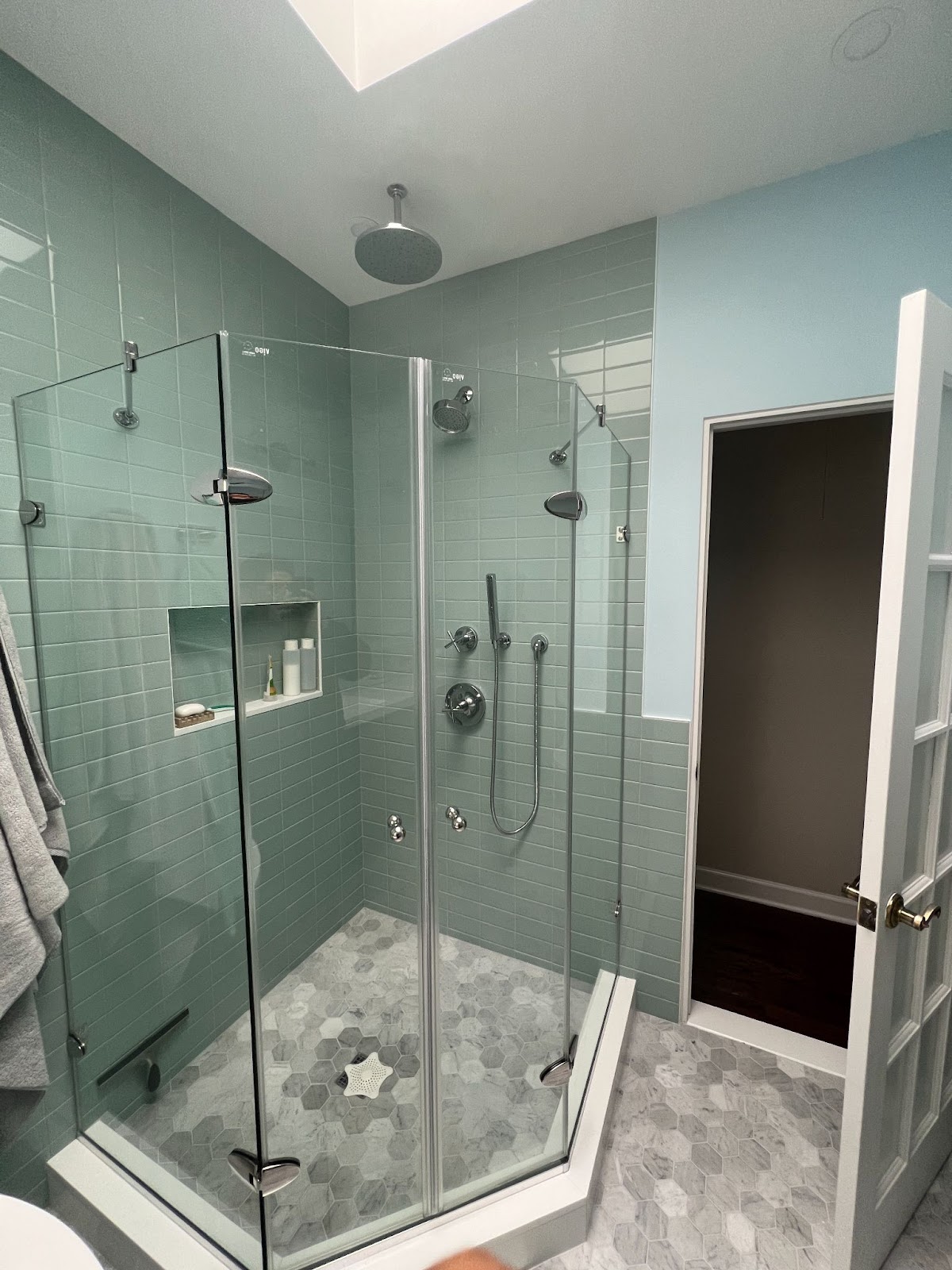 Shower stall with green wall tile, blue paint, hexagonal gray flooring, polished chrome hardware, and a skylight