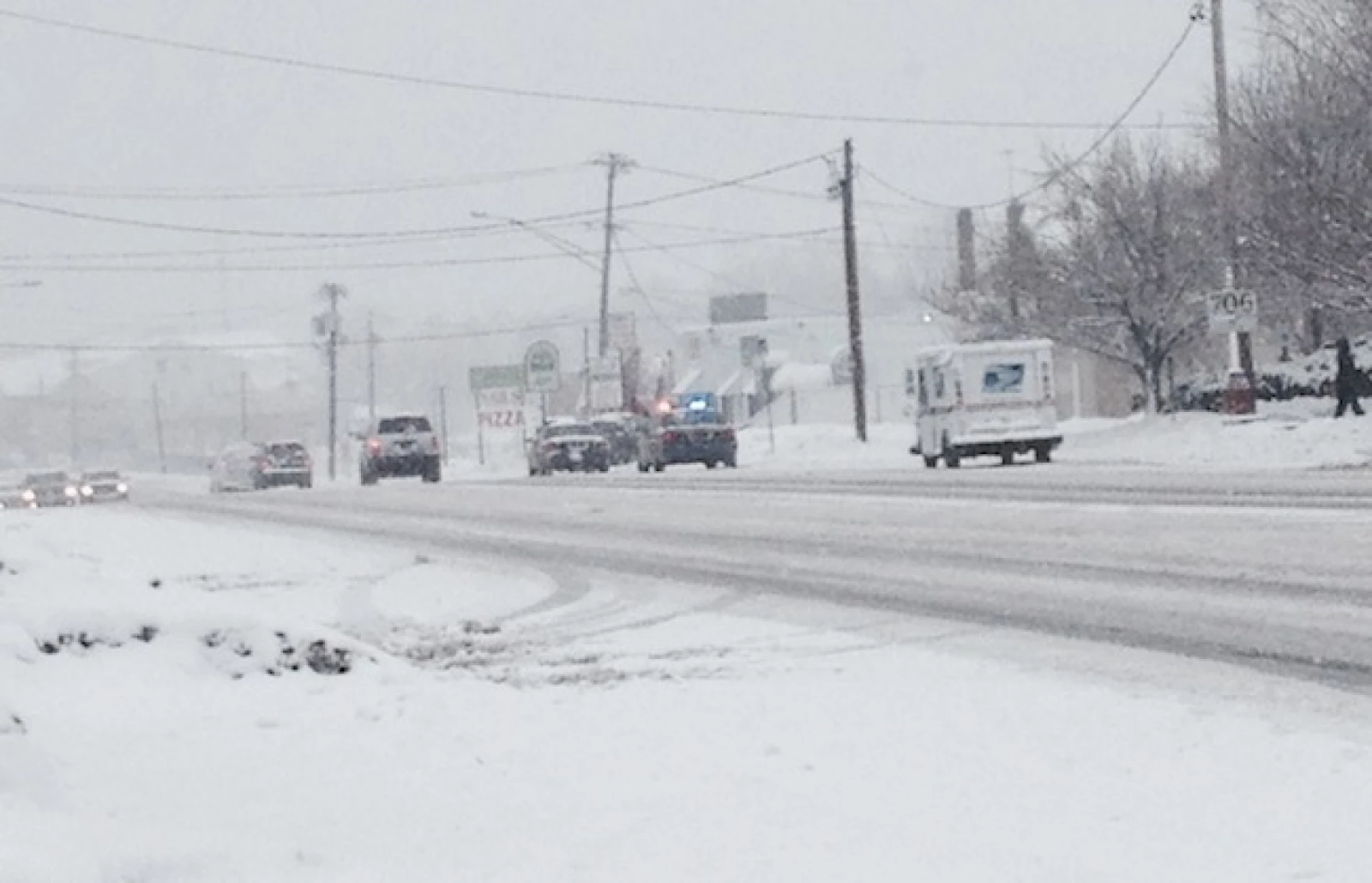 A snow-covered road with civilian and first responder vehicles