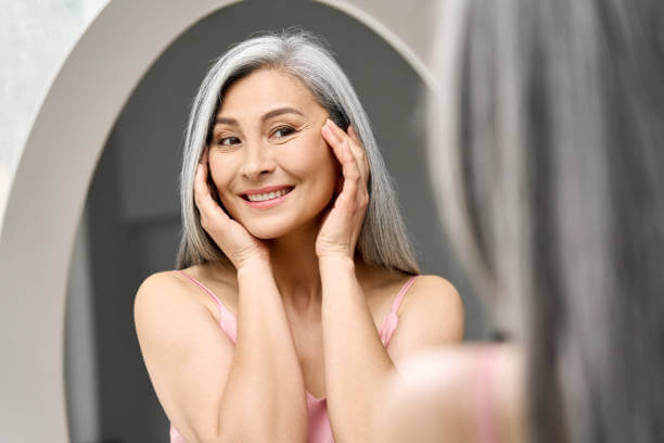 An aging woman gazing at herself in the mirror with a warm smile, embracing self-care and the benefits of anti-aging supplements for a youthful glow.