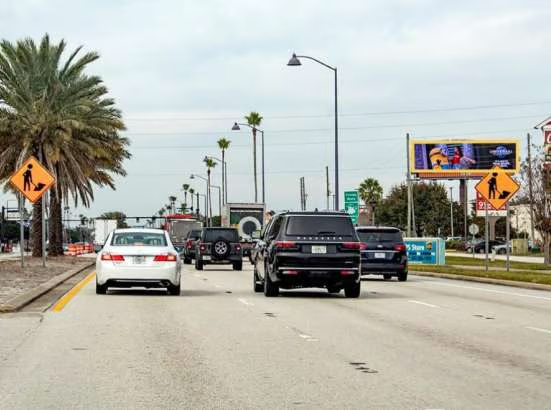 Cars driving on a road with palm trees and a billboard in the distance