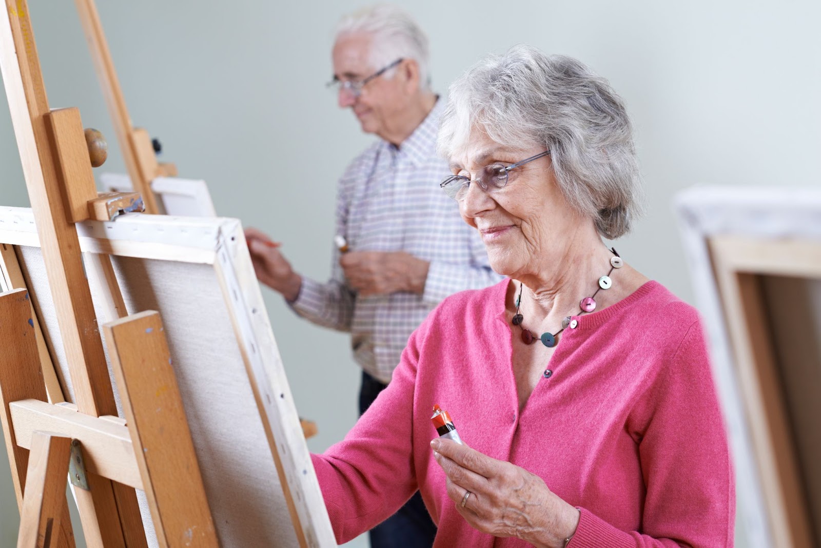 A smiling senior participates in a painting class with other older adults.