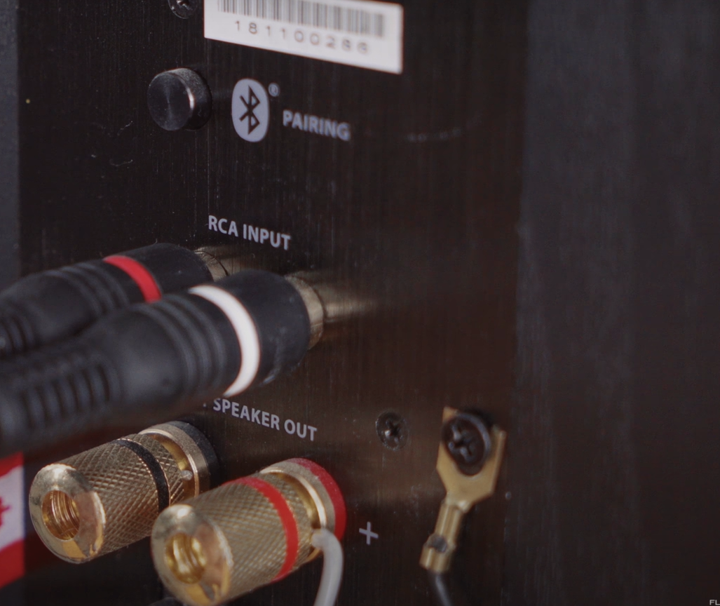 Close-up of RCA input, speaker output, and Bluetooth pairing button on an audio amplifier.