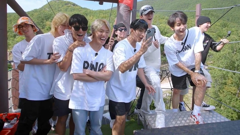 a group photo of the Seventeen members on a zipline platform in Italy. They are all smiling or laughing.