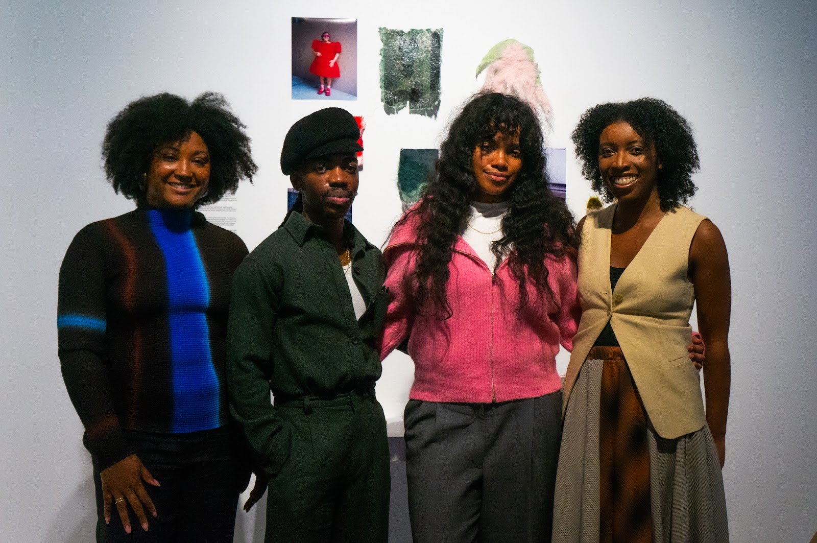 Four individuals pose in front of a gallery wall, smiling into the camera. 