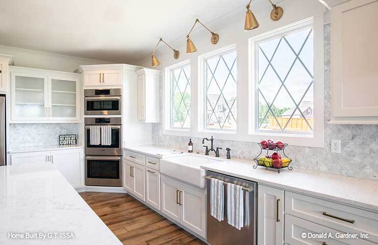 The kitchen includes stainless steel appliances, a farmhouse sink, and three-paneled windows.