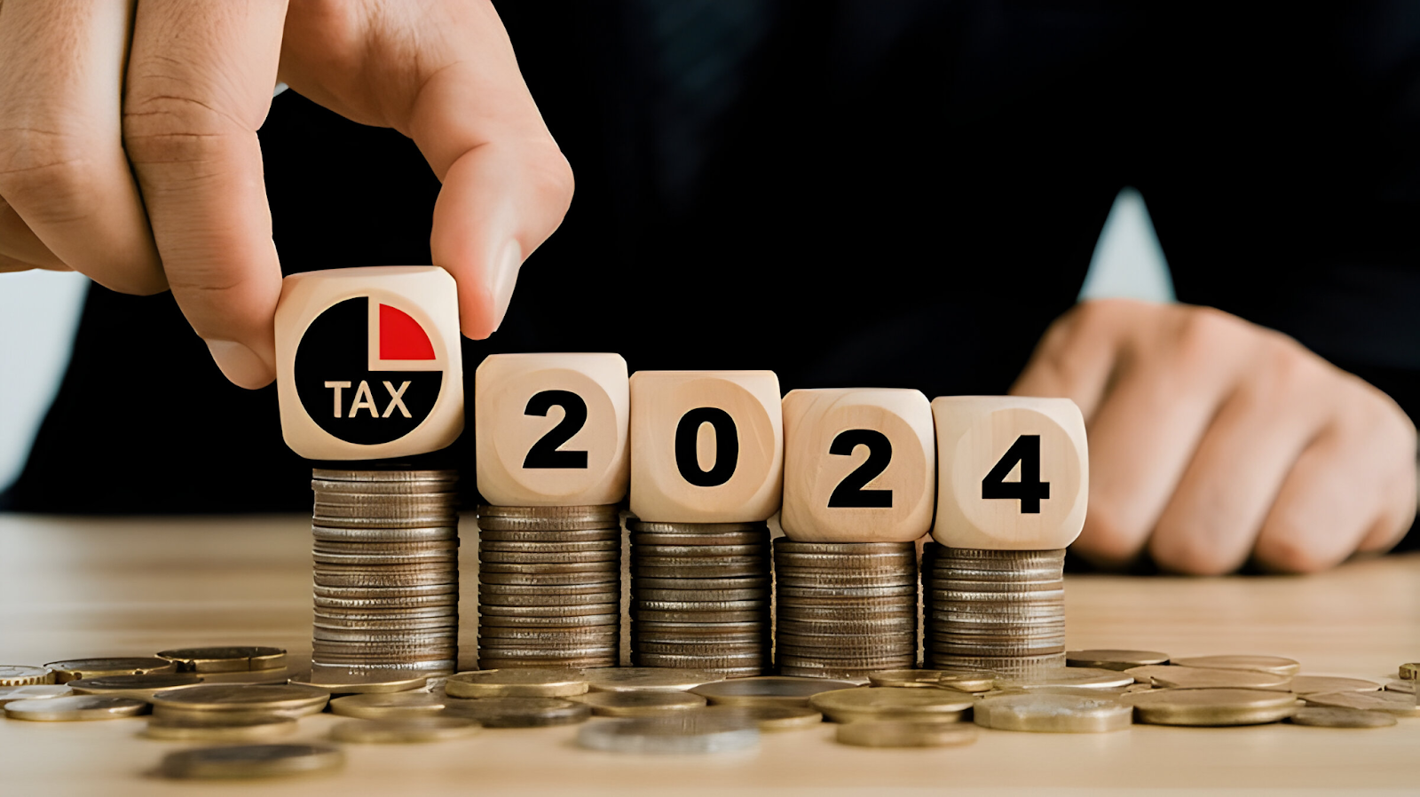 Hand placing a tax cube on stacked coins with wooden blocks displaying '2024,' symbolizing tax planning and financial strategy for the year.