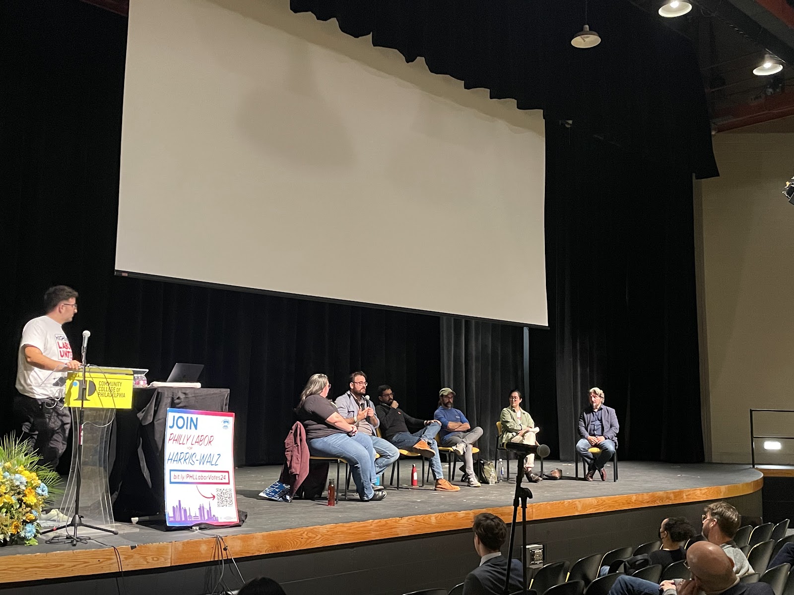 Photograph of HELU town hall on stage at the Community College of Philadelphia. From right to left, Todd Wolfson, AAUP, Levin Kim, HELU/UAW 4121, Jamie Zigarelli (FSFCCP), Jesús Fernández (TUGSA), Evan Kassof (Phila. AFL-CIO), Danielle Scherer (TAUP).