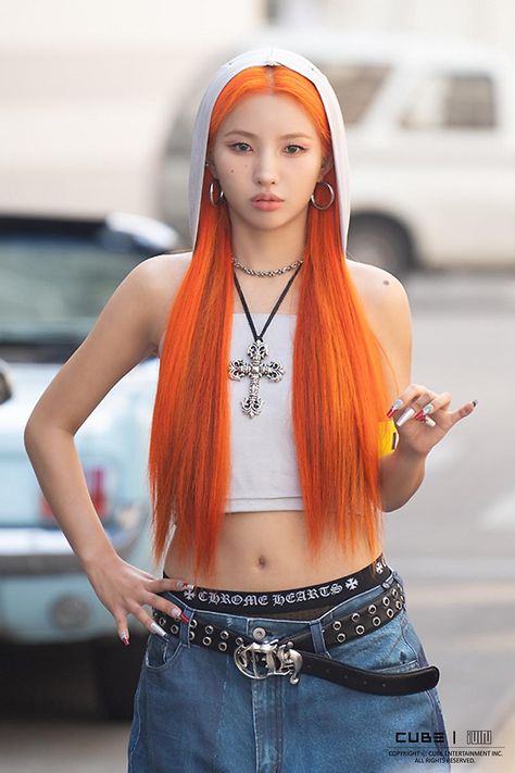 A picture of Soyeon with a long orange hair wearing a white crop top and blue jean trouser  