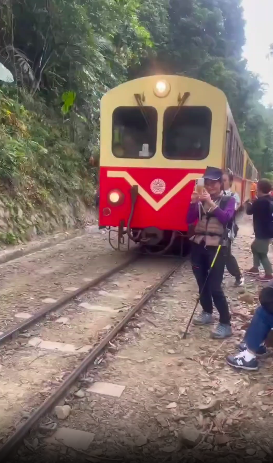 This contains an image of a woman  standing perilously close to the tracks, engrossed in taking photos.