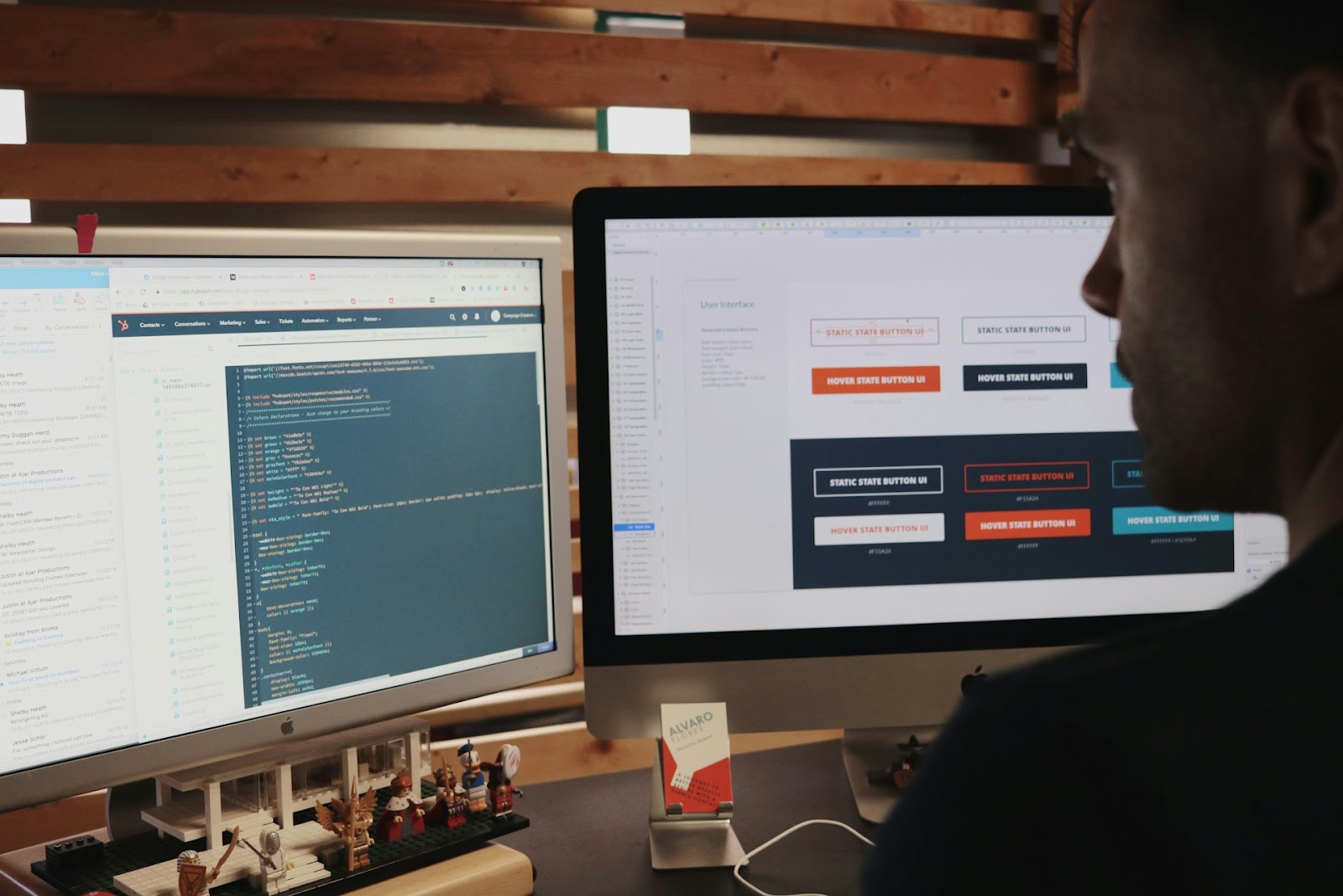 A person working on a computer with dual monitors, displaying code on one screen and user interface design with button states on the other, focused on developing and designing web elements.