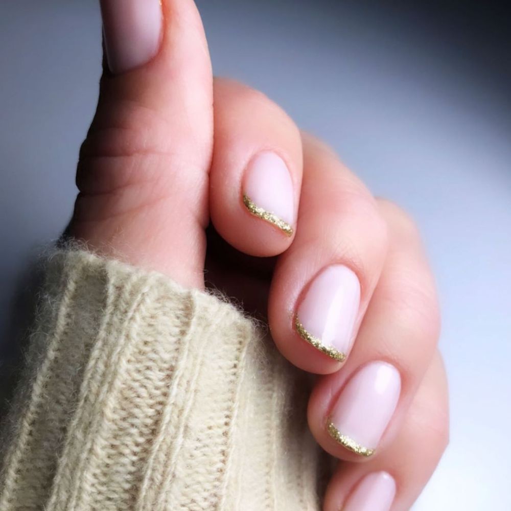 Zoom in view of hand with simple French tip nail having Gold sparkle micro French tips