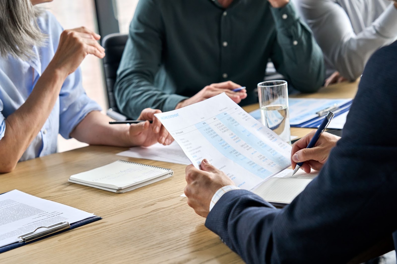 Mãos masculinas de perto fazendo anotações no relatório financeiro na reunião de mesa.