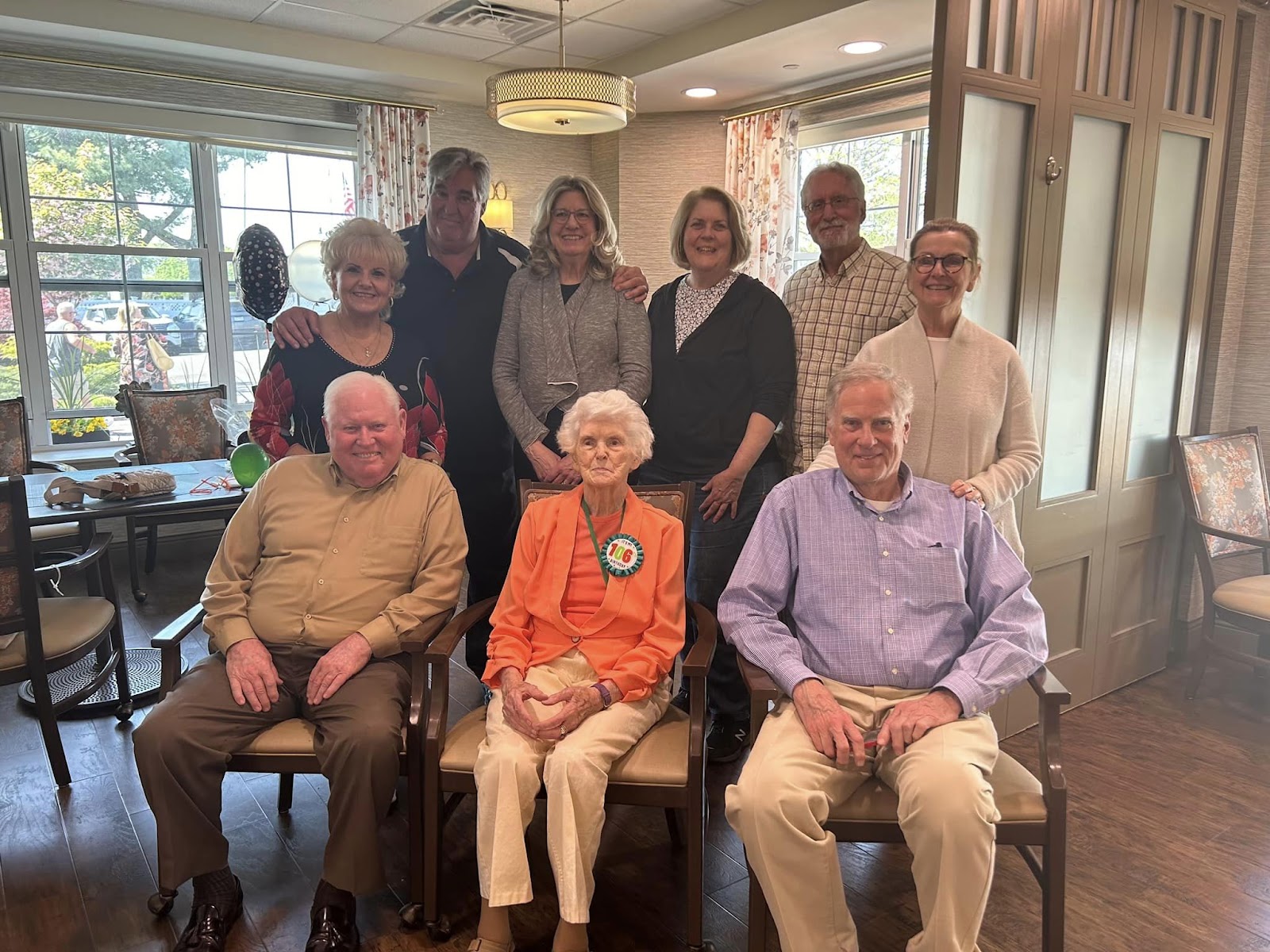 A group of seniors sitting in chairs and standing behind those sitting in chairs, all of whom are smiling at the camera