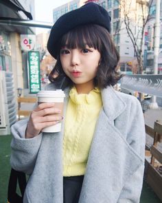 This  contain an image of Hong Young Gi holding a coffee cup and wearing a gray coat with black trims