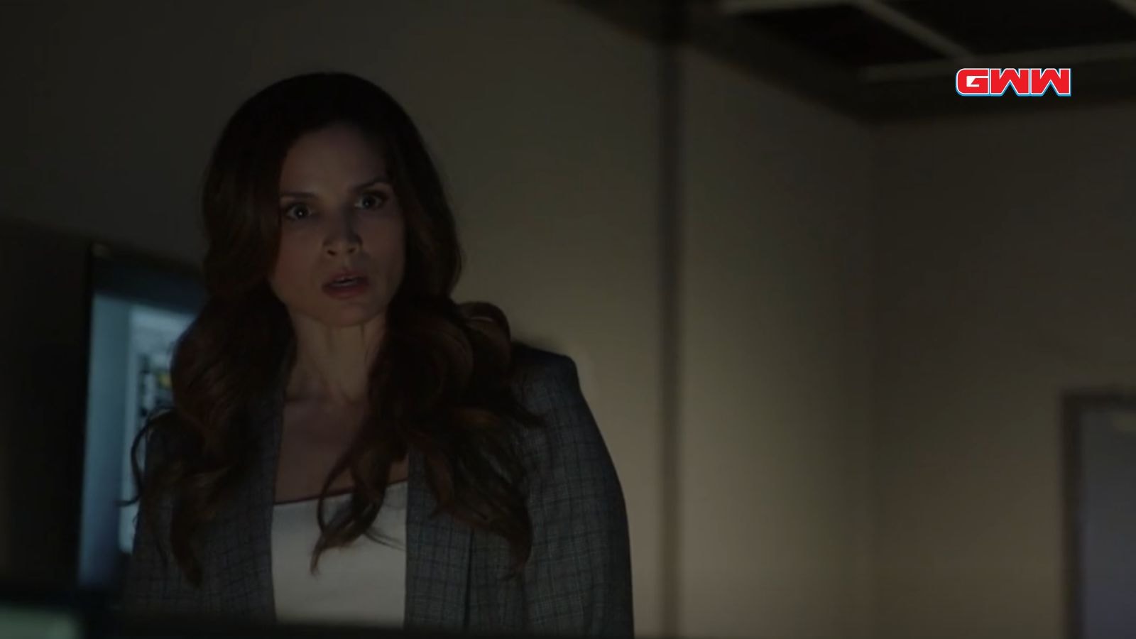 A surprised Agent Jessica Knight with long brown hair in a dimly lit room.