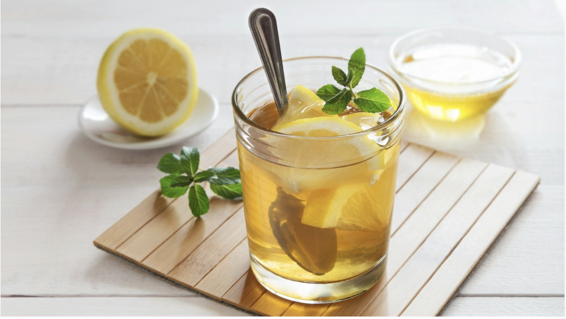 A glass of full of the Krupnik Honey Punch drink with lemon, honey, mint, and a silver spoon
