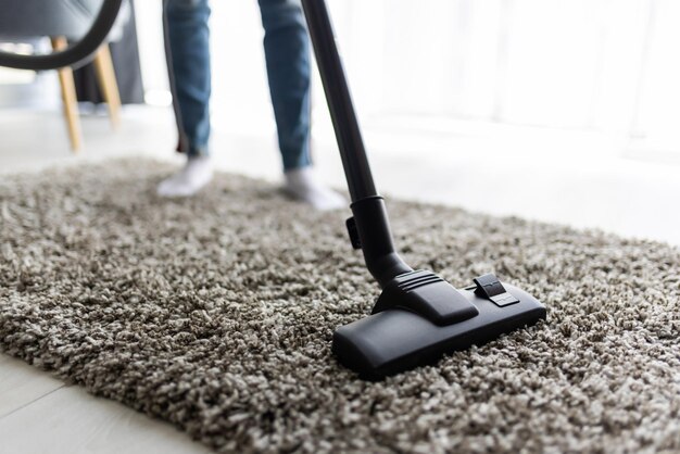 People, housework and housekeeping concept - close up of woman with legs vacuum cleaner cleaning carpet at home