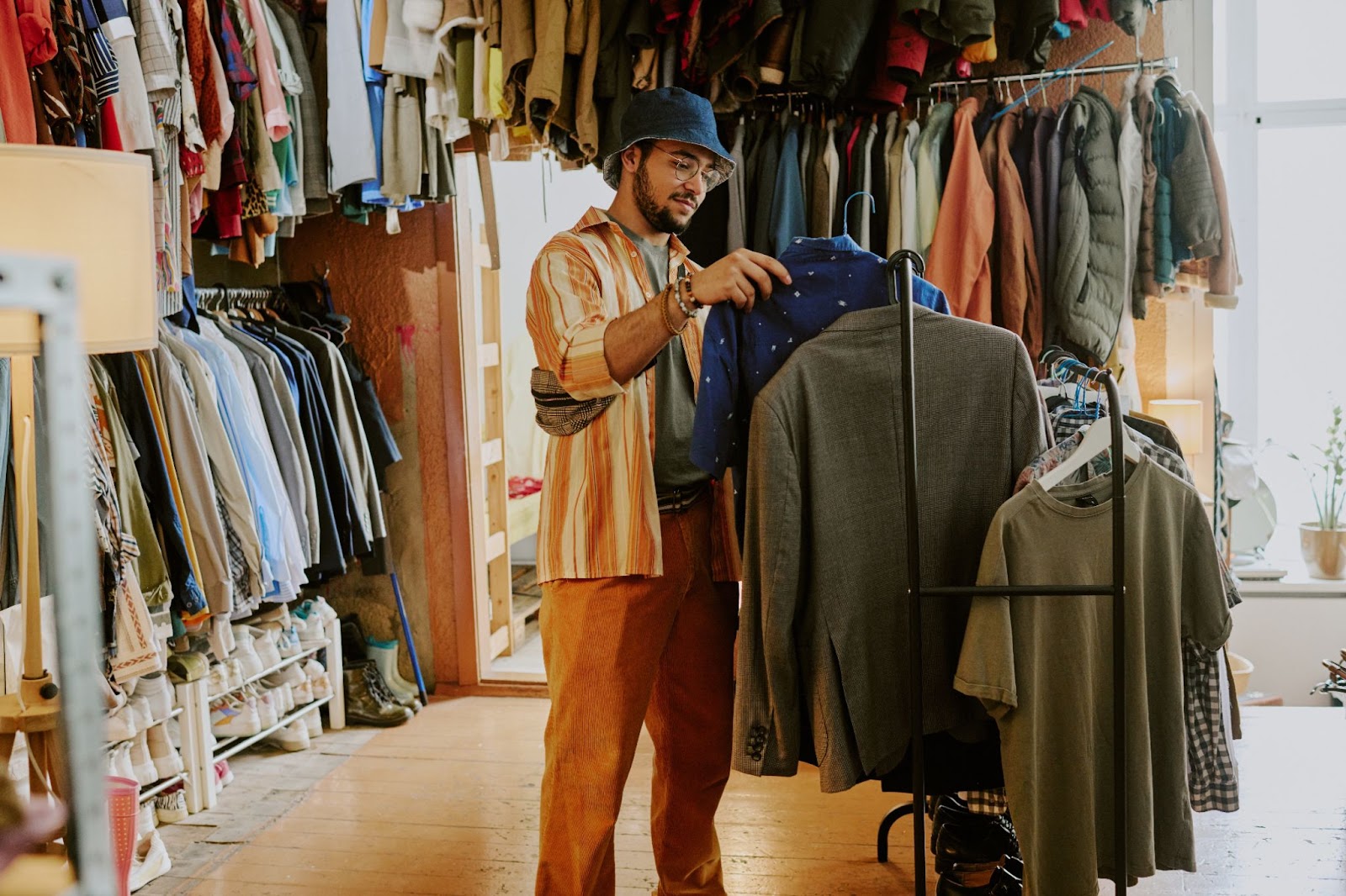 Person browsing clothes in a cozy vintage thrift shop filled with various garments and accessories hanging on racks