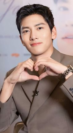 This contains an image of: Ji Chang Wook on a coffee brown suit making a heart sign 