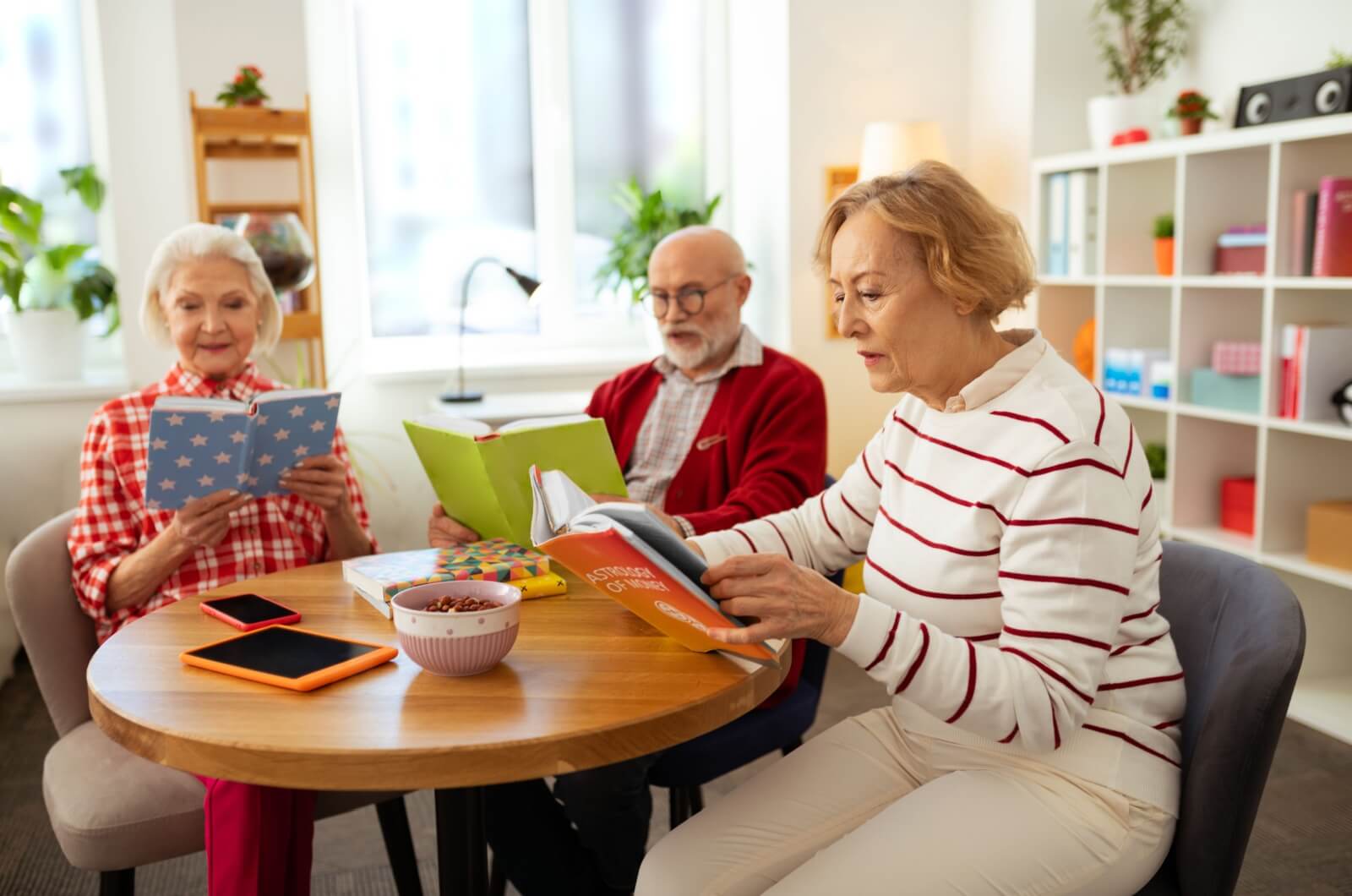 A group of older adults sitting at a table reading books.
