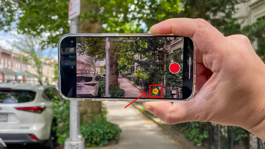 A hand holding an iPhone horizontally, shooting a spatial video, the spatial video mode enabling button is highlighted in red