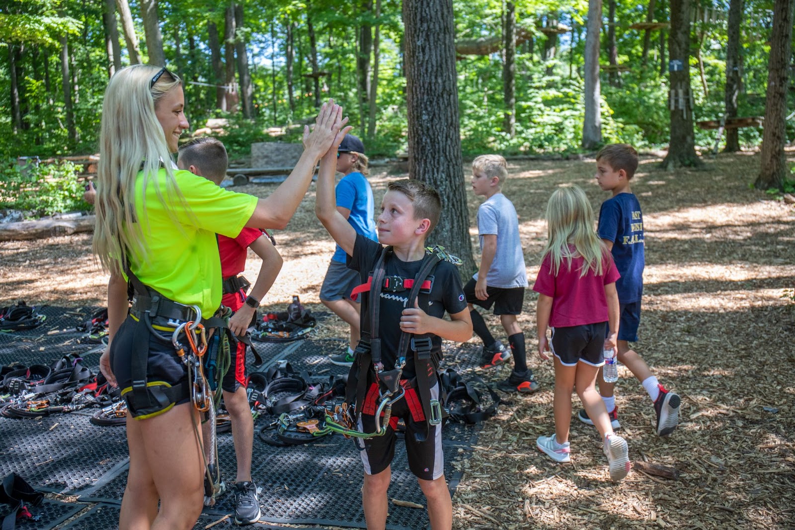 A woman and a group of kids preparing for a zip line adventure at TreEscape Aerial Adventure Park, wearing helmets and harnesses.