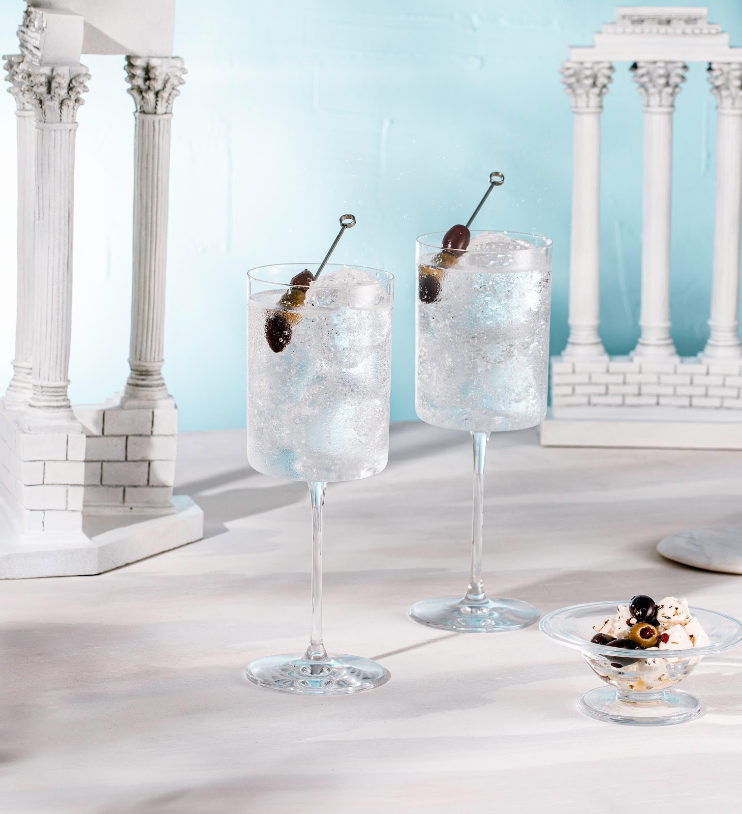 Two glasses of liquid with ice and a spoon on top of a small bowl.

