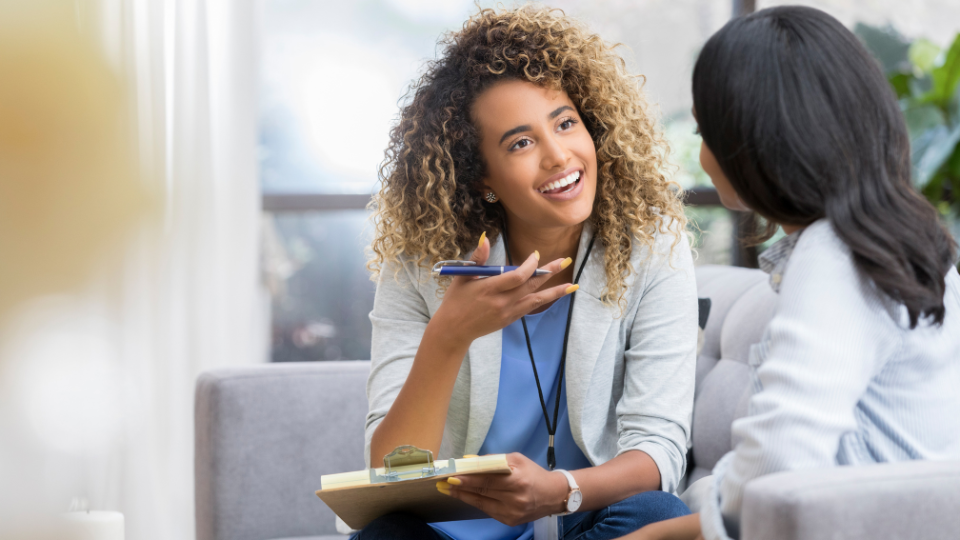 Une conseillère souriante discute avec une cliente lors d'une consultation, tenant un stylo et un bloc-notes pour prendre des notes.