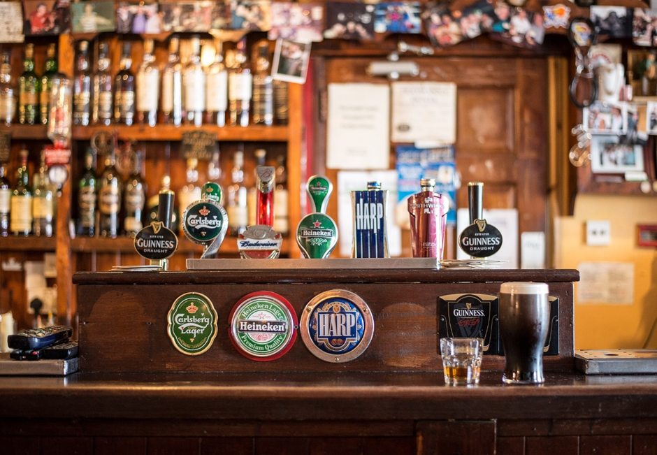 Wooden pub bar with beer taps and liquor bottles in the background.