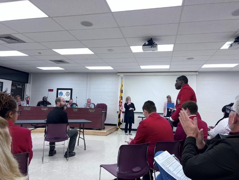 board room photo of man reading off names