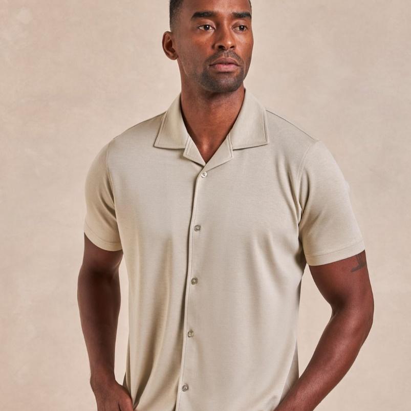 A man is posing in a tan short-sleeved button-up.