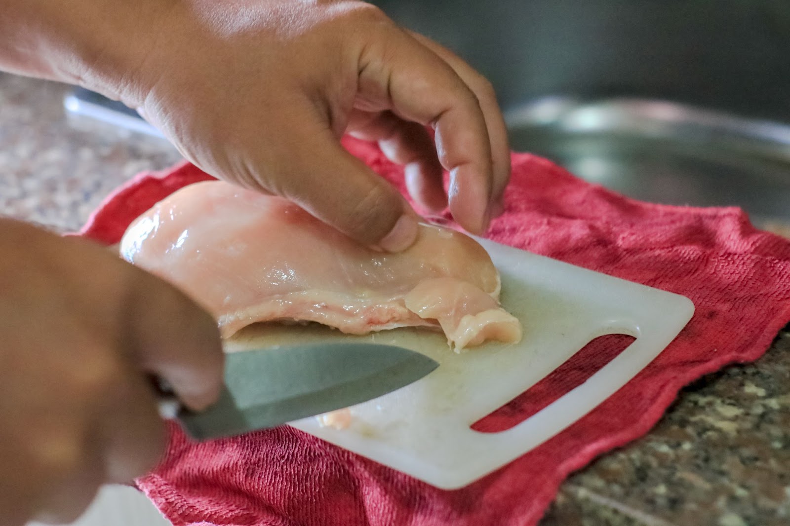 cutting chicken breast into thin slices to prepare chicken cutlets