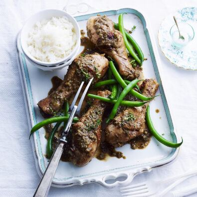A serving tray with jerk-seasoned chicken drumsticks, fresh green beans, and a side of white rice, presented on a white table setting.