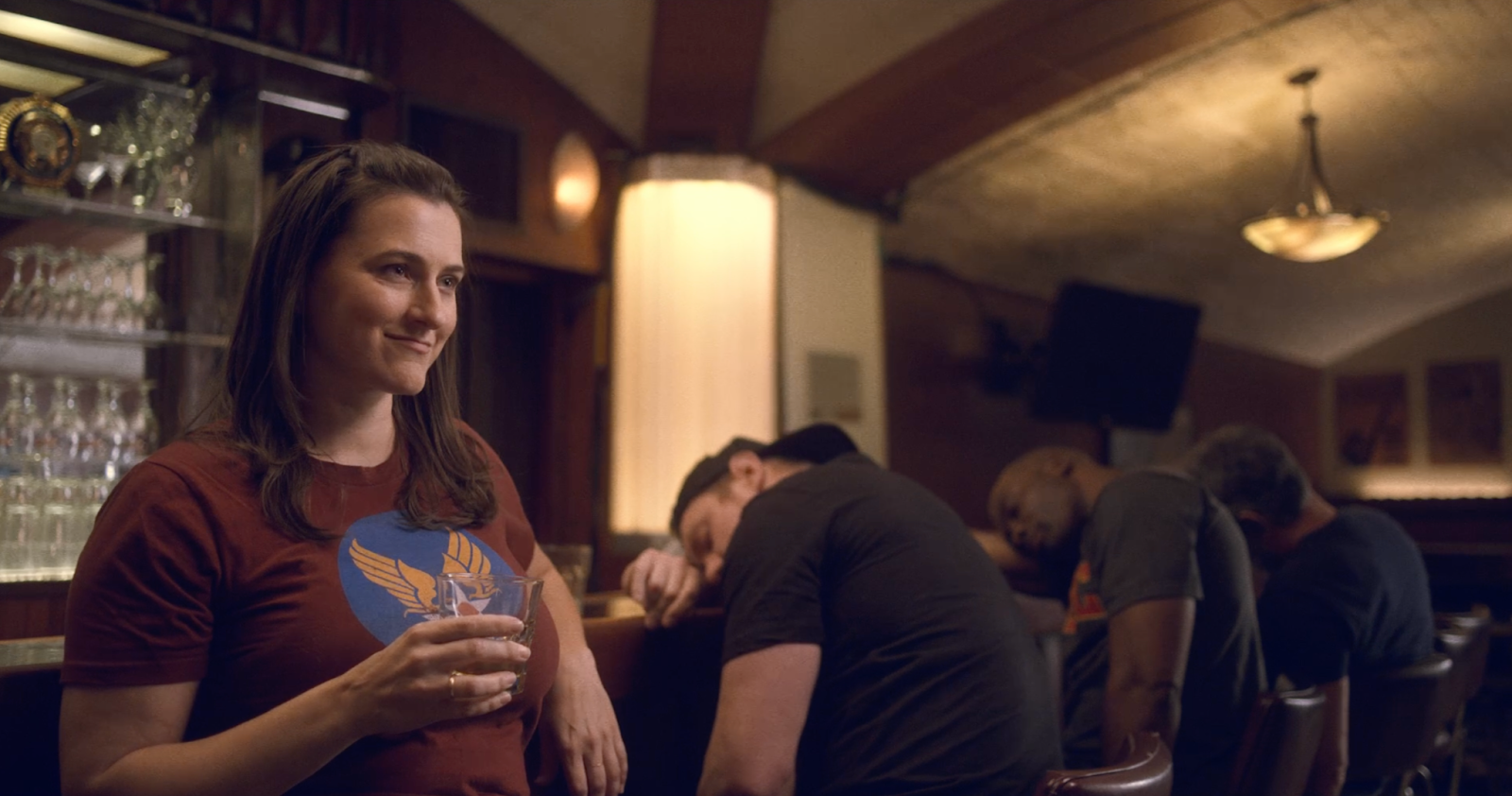 A woman drinks at the bar while everyone else sleeps