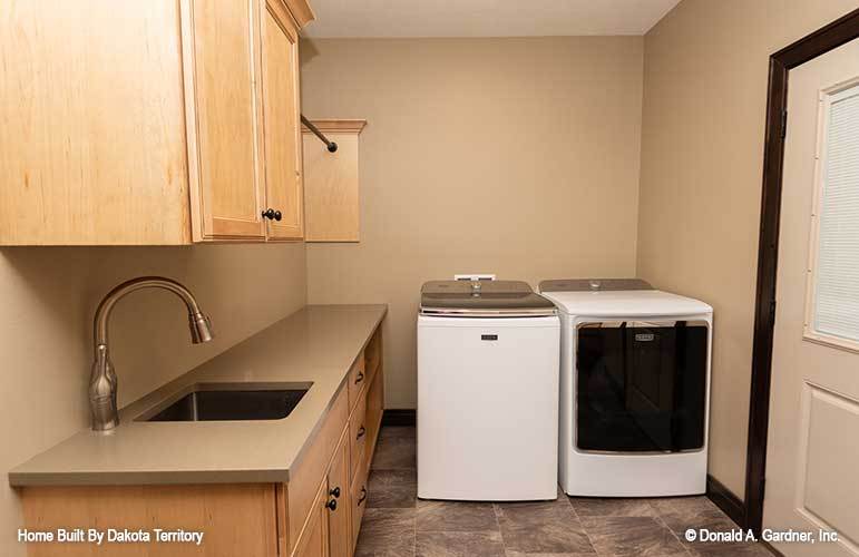 Laundry room with white appliances, wooden cabinetry, and a utility sink.