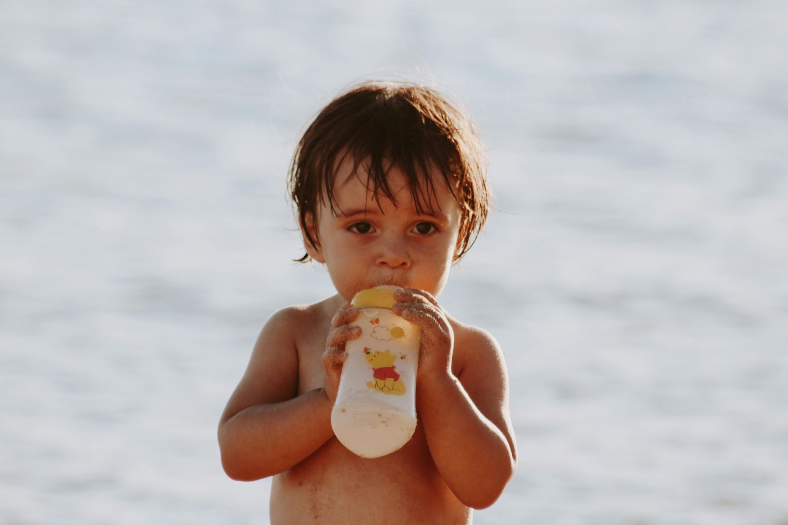 A Toddler Drinking Milk from the Baby Bottle while on the Beach