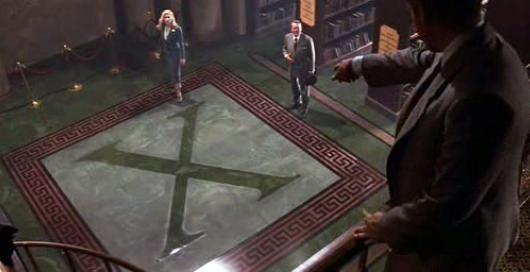 Indiana Jones points from the top floor of the library at the giant “X” on the floor beneath the feet of Elsa and Brody. 