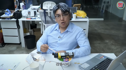 A picture of Gwak Beom on a sky blue shirt sitting in front of a table talking 