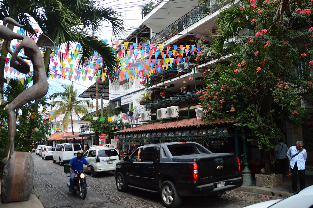 Cars parked on the streets and a man on a bike on the street and decorated with paper flags 