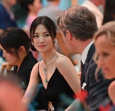 This contains an image of Song Hye Kyo    in a black dress sitting next to other people