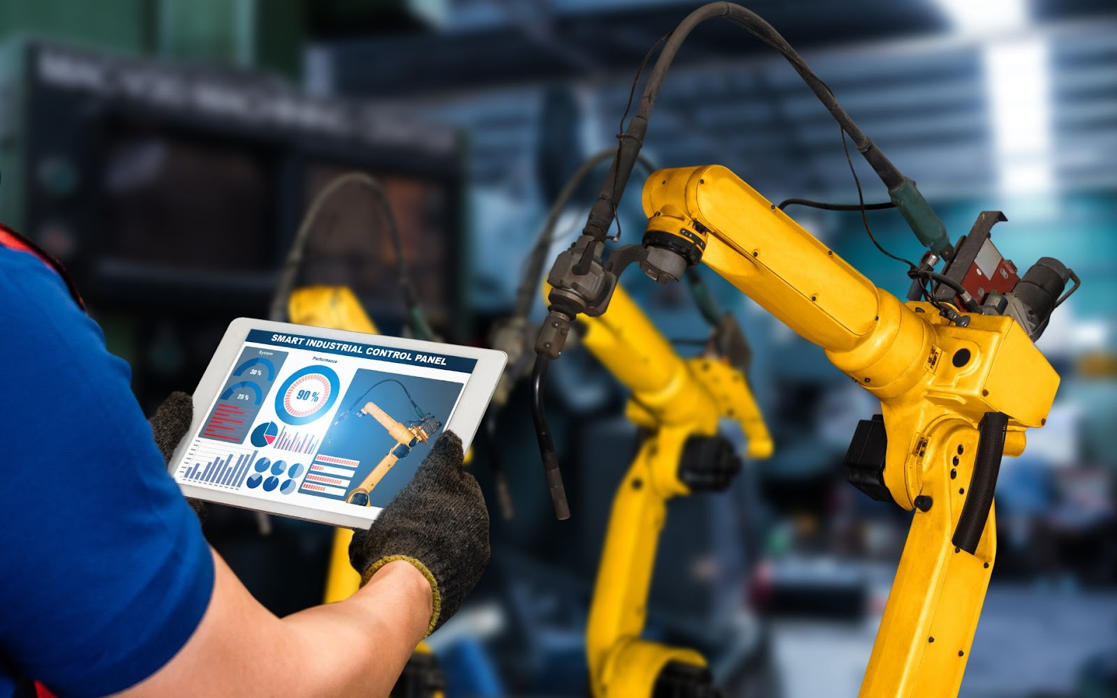 Worker using a tablet to control robotic arms in an automated industrial environment.