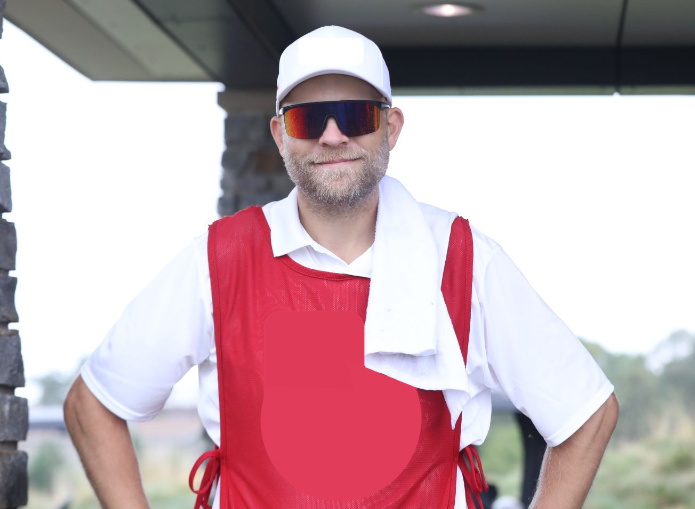 Brett Jones standing on a golf course in his caddy bib and hat, ready to serve with a smile.