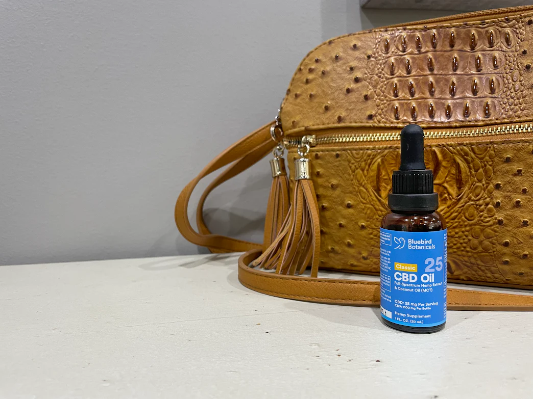 Bluebird Botanicals Classic 10mg CBD oil bottle placed beside a purse for daily wellness use