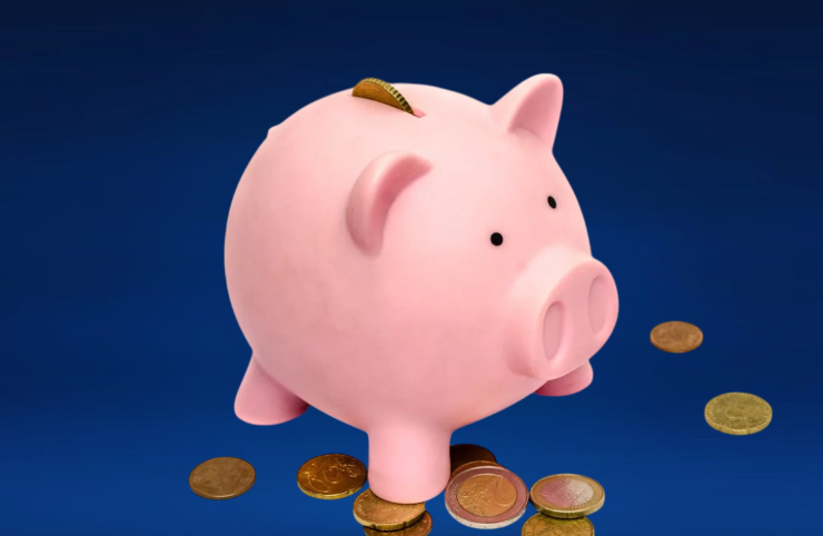 Dark blue background featuring a pink piggy bank with a coin being inserted and euro coins scattered on the floor