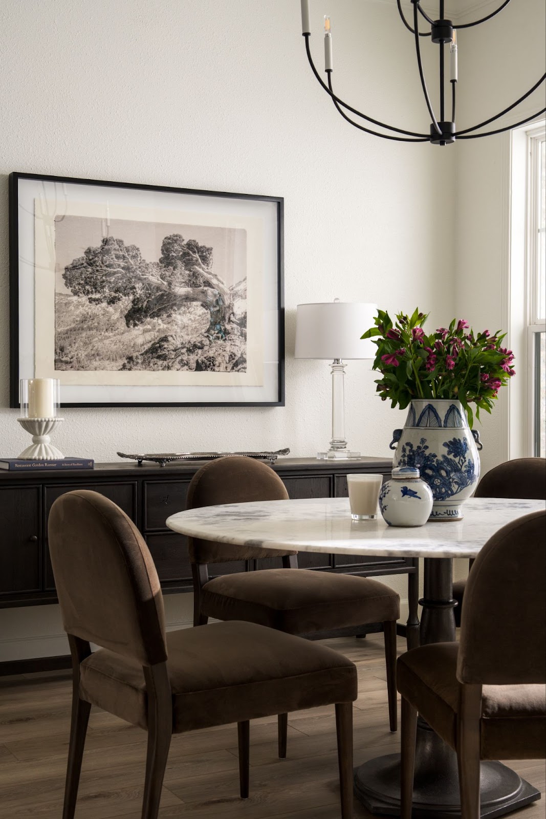 Dining room design with brown chairs showing a piece of artwork hung above a sideboard in the background, showing the height to hang a picture above furniture
