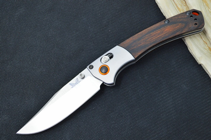 An image showing the Benchmade Mini Crooked River manual folding knife. The knife features a clip point blade and an ergonomic Dymondwood handle with stainless liners.