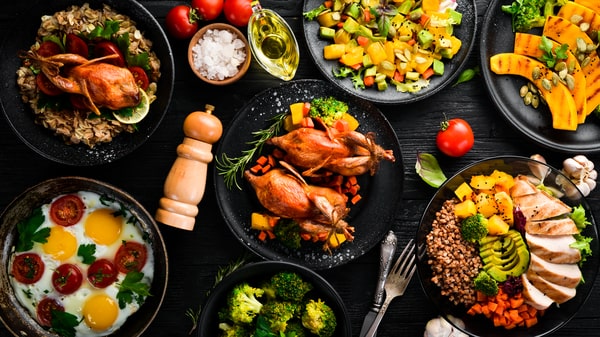 A display of various gourmet dishes, including roasted quail, grilled vegetables, eggs, and fresh greens, with some components prepared using an Instant Pot, all arranged on dark plates