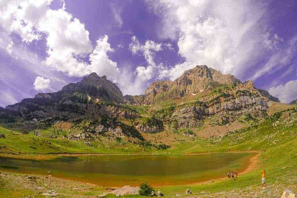 Ibón de montaña en el Valle de Tena rodeado de cumbres pirenaicas y praderas verdes

